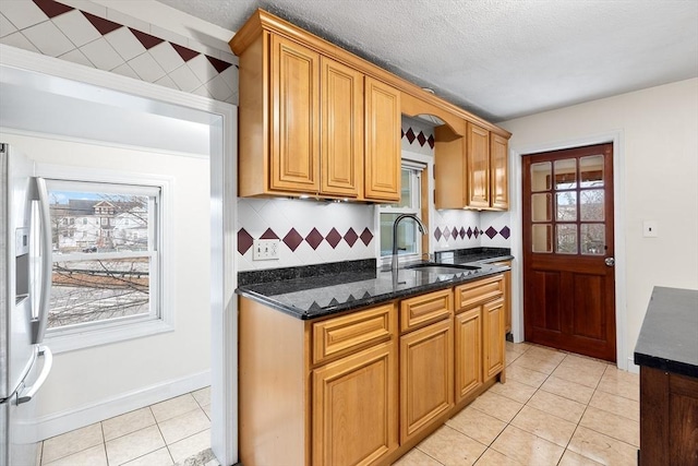 kitchen featuring decorative backsplash, stainless steel refrigerator with ice dispenser, sink, light tile patterned floors, and dark stone countertops