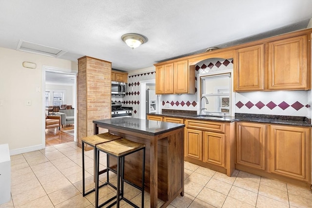 kitchen with appliances with stainless steel finishes, backsplash, light tile patterned floors, and sink