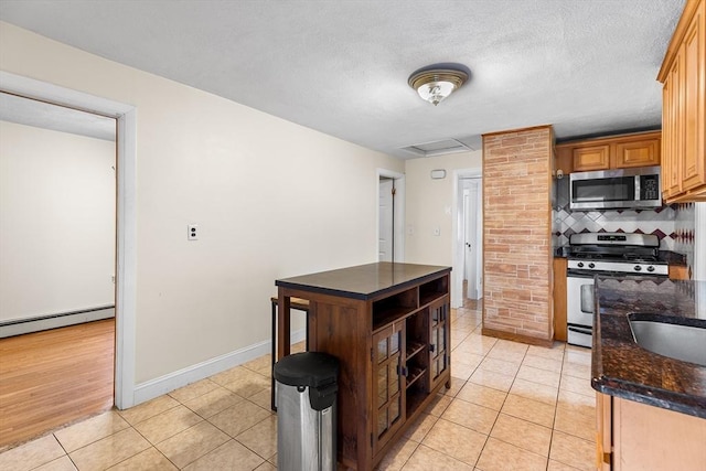 kitchen with baseboard heating, decorative backsplash, light tile patterned floors, and stainless steel appliances