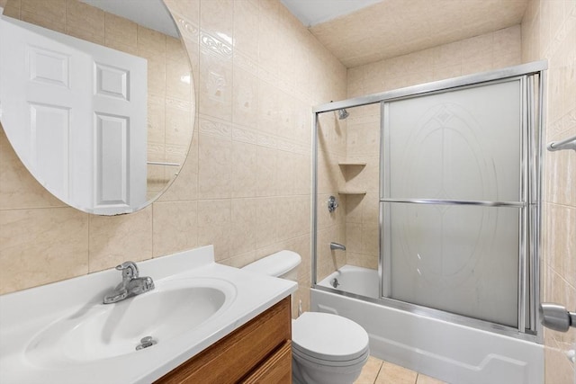 full bathroom with combined bath / shower with glass door, tile patterned floors, toilet, vanity, and tile walls