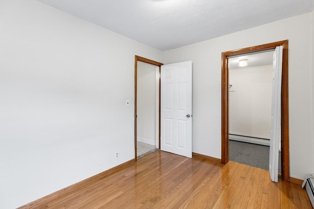 unfurnished bedroom featuring baseboard heating, a closet, and light hardwood / wood-style floors