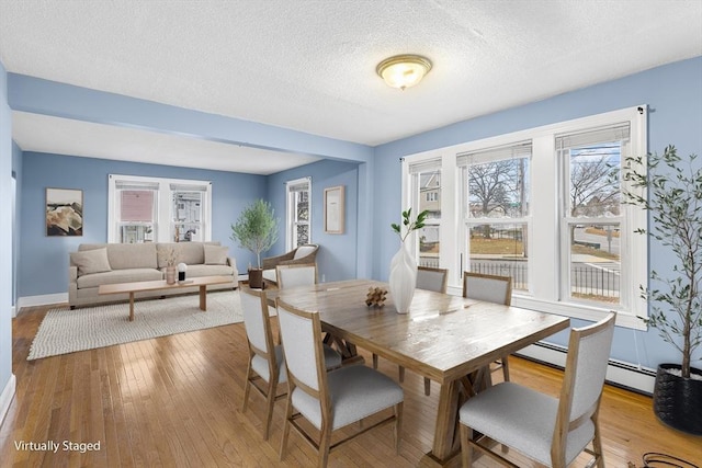 dining room with light hardwood / wood-style floors, a textured ceiling, and a baseboard heating unit