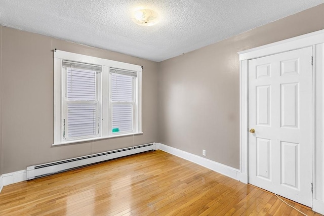 empty room with hardwood / wood-style flooring, a textured ceiling, and a baseboard radiator