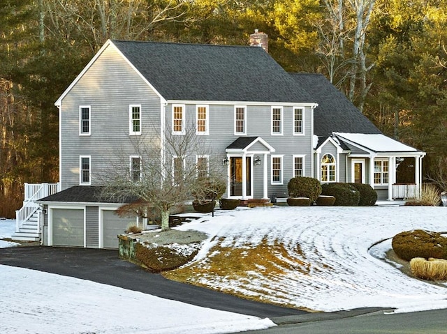 colonial inspired home with roof with shingles, driveway, a chimney, and an attached garage