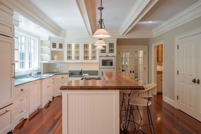 kitchen with sink, butcher block counters, hanging light fixtures, a center island with sink, and french doors