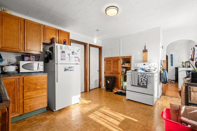178 Cohasset St, Worcester, MA 01604 - kitchen featuring white appliances, arched walkways, brown cabinetry, and dark countertops