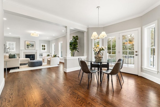 dining space featuring dark wood-style flooring, an inviting chandelier, a glass covered fireplace, and crown molding