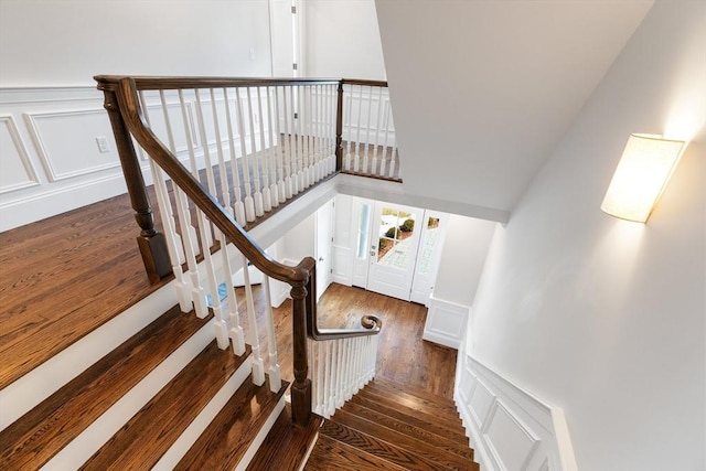 stairway with a wainscoted wall, a decorative wall, and wood finished floors