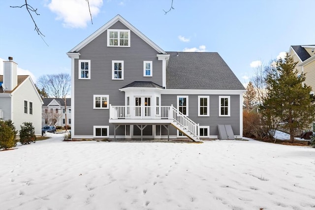 snow covered back of property with a deck and stairs