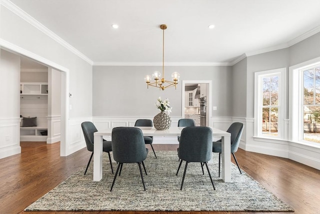 dining room with crown molding, dark wood-type flooring, wainscoting, and a notable chandelier