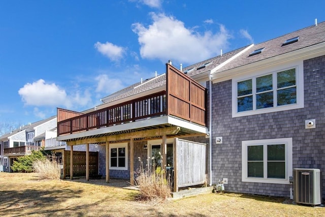 rear view of property with cooling unit, a wooden deck, and roof with shingles