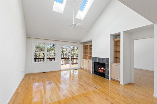 unfurnished living room with high vaulted ceiling, built in features, light wood-style floors, a skylight, and a tile fireplace