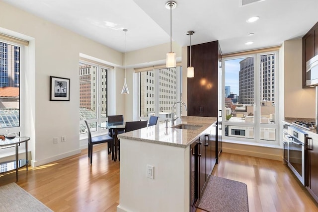 kitchen with dark brown cabinets, a sink, stainless steel oven, light wood-type flooring, and cooktop