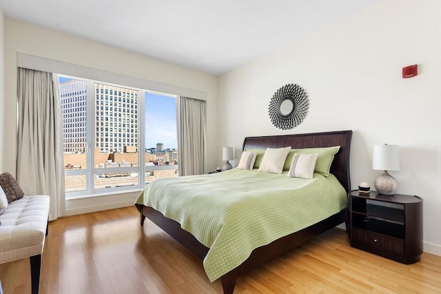 bedroom with baseboards, a city view, and light wood-style flooring