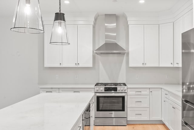 kitchen featuring white cabinets, decorative light fixtures, wall chimney range hood, and appliances with stainless steel finishes