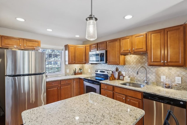 kitchen with sink, hanging light fixtures, appliances with stainless steel finishes, and light stone counters