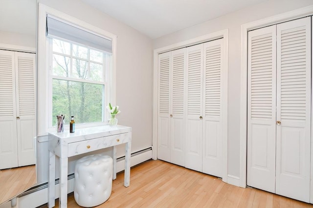 bedroom featuring multiple closets, a baseboard radiator, and light wood finished floors