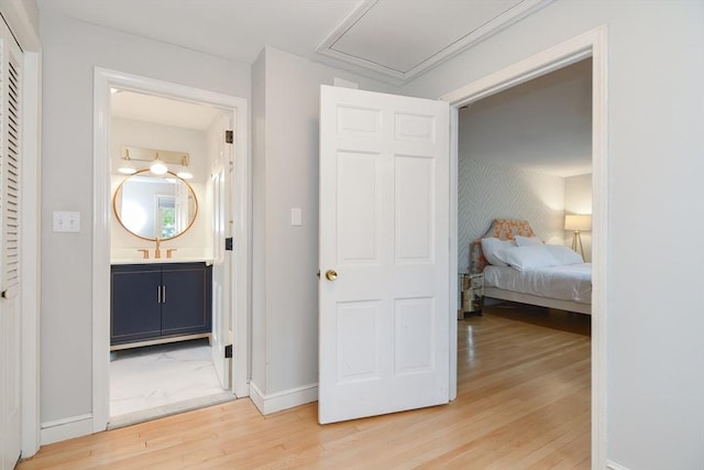 bedroom with light wood finished floors, a sink, baseboards, connected bathroom, and attic access