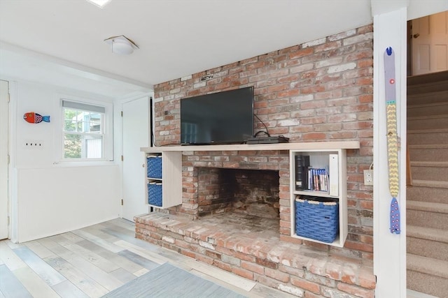unfurnished living room featuring stairway, a brick fireplace, and wood finished floors