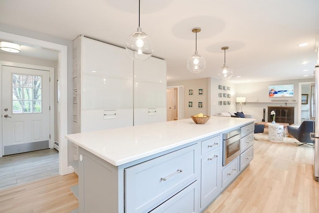 kitchen featuring light wood-style floors, stainless steel microwave, hanging light fixtures, and a kitchen island