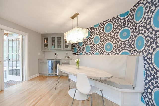 dining space with wine cooler, bar with sink, light wood-type flooring, baseboards, and a chandelier
