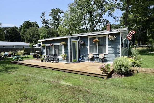 rear view of house with a deck, a chimney, a yard, and fence