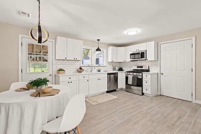 kitchen with backsplash, hanging light fixtures, appliances with stainless steel finishes, light hardwood / wood-style floors, and white cabinetry