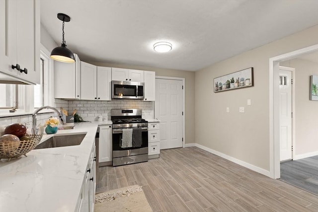 kitchen featuring light wood-type flooring, stainless steel appliances, sink, pendant lighting, and white cabinets