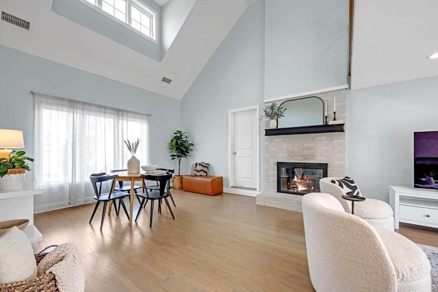 dining area featuring a brick fireplace, light wood-style floors, visible vents, and a towering ceiling