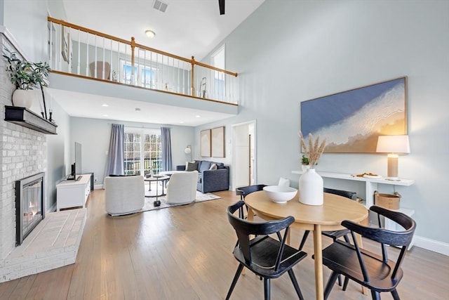 dining room featuring visible vents, wood finished floors, a high ceiling, a fireplace, and baseboards