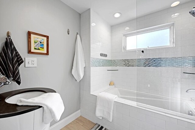 bathroom featuring wood finished floors, tiled shower / bath, and baseboards