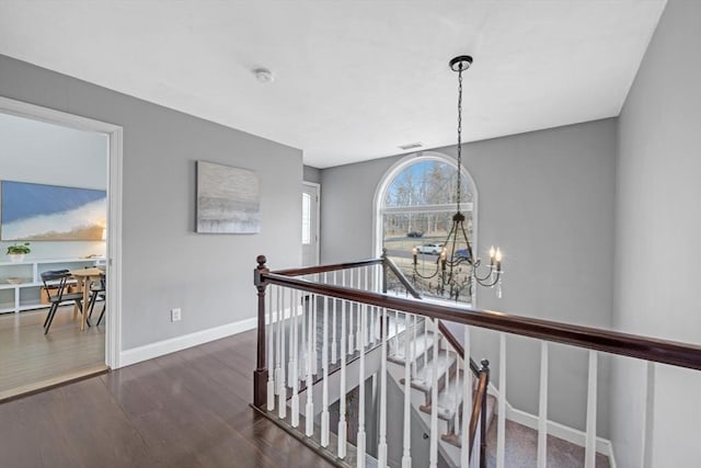 corridor featuring visible vents, baseboards, an upstairs landing, an inviting chandelier, and dark wood-style flooring