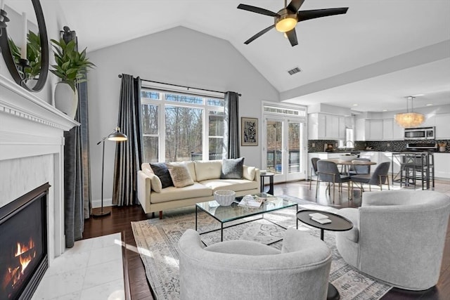 living area with a ceiling fan, visible vents, high vaulted ceiling, a lit fireplace, and french doors