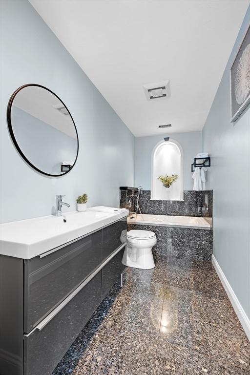 full bath featuring vanity, baseboards, granite finish floor, toilet, and a washtub