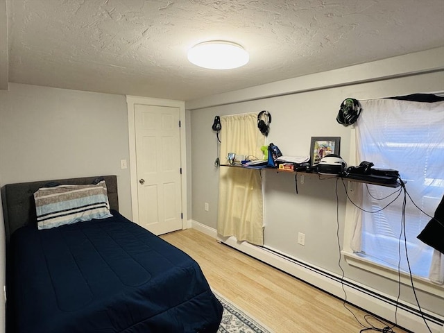 bedroom with baseboard heating, a textured ceiling, light wood-type flooring, and baseboards