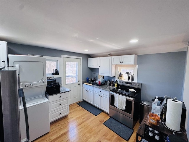 kitchen featuring light wood-style flooring, stainless steel electric range, stacked washing maching and dryer, white cabinets, and a sink