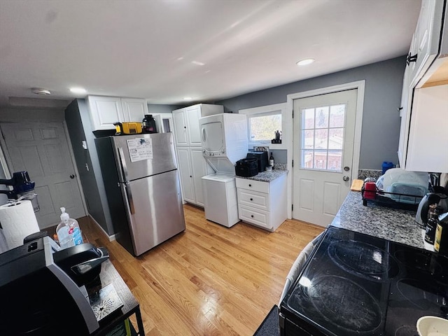 kitchen featuring light wood-style flooring, white cabinetry, freestanding refrigerator, light countertops, and stacked washer / dryer