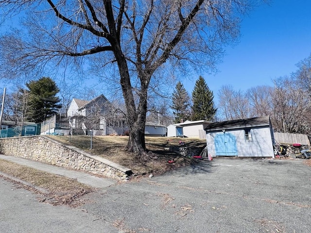 view of front of property featuring aphalt driveway, a shed, an outdoor structure, and fence