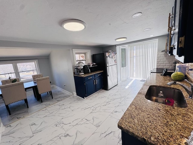 kitchen with baseboards, freestanding refrigerator, marble finish floor, blue cabinets, and a sink