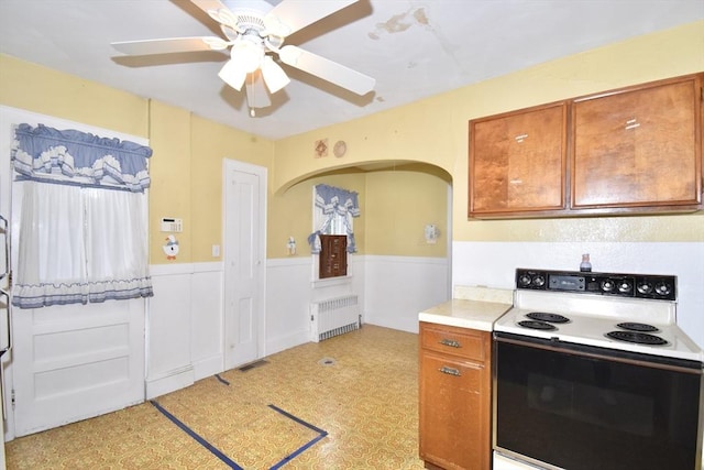 81 Osborne Ter, Springfield, MA 01104 - kitchen with white range with electric stovetop, radiator heating unit, ceiling fan, wainscoting, and brown cabinetry