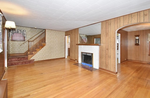 81 Osborne Ter, Springfield, MA 01104 - unfurnished living room featuring wood finished floors, arched walkways, a fireplace with flush hearth, stairs, and wood walls