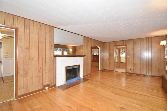 81 Osborne Ter, Springfield, MA 01104 - unfurnished living room featuring arched walkways, wood finished floors, a fireplace with flush hearth, wood walls, and plenty of natural light