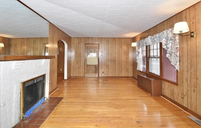 81 Osborne Ter, Springfield, MA 01104 - unfurnished living room with radiator heating unit, wood walls, wood finished floors, a fireplace with flush hearth, and arched walkways