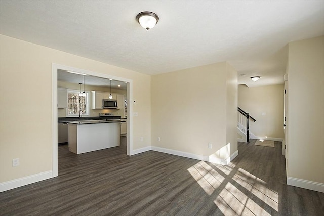 unfurnished living room featuring dark wood finished floors, baseboards, and a sink