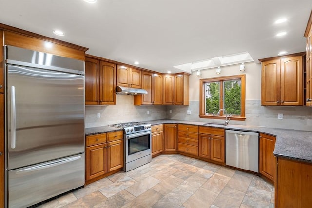 103 Randlett Park, Newton, MA 02465 - kitchen featuring appliances with stainless steel finishes, under cabinet range hood, a skylight, tasteful backsplash, and brown cabinets