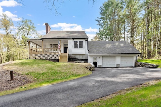 view of front of home with a chimney, driveway, a porch, a garage, and a front lawn
