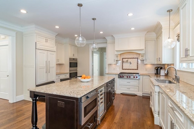 kitchen featuring sink, hanging light fixtures, a center island, built in appliances, and light stone counters