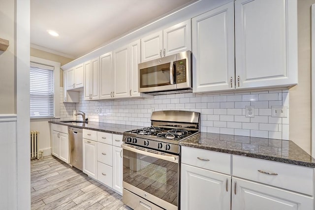 kitchen with white cabinetry, stainless steel appliances, radiator, and dark stone counters