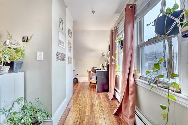 hallway with a baseboard heating unit, wood-type flooring, and a healthy amount of sunlight