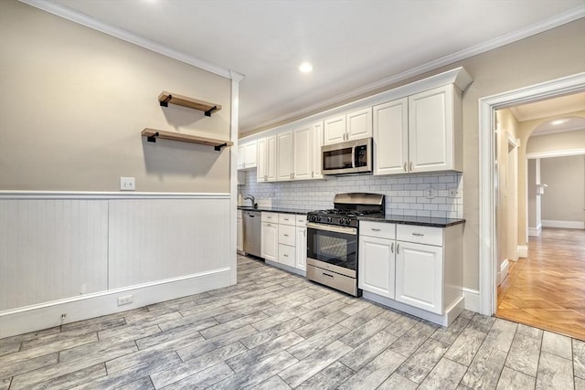 kitchen with white cabinetry, crown molding, light wood-type flooring, stainless steel appliances, and backsplash